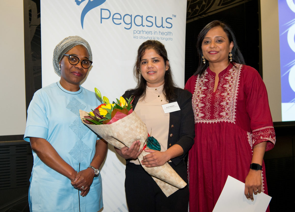 three women, middle is award recipient with bouquet of flowers